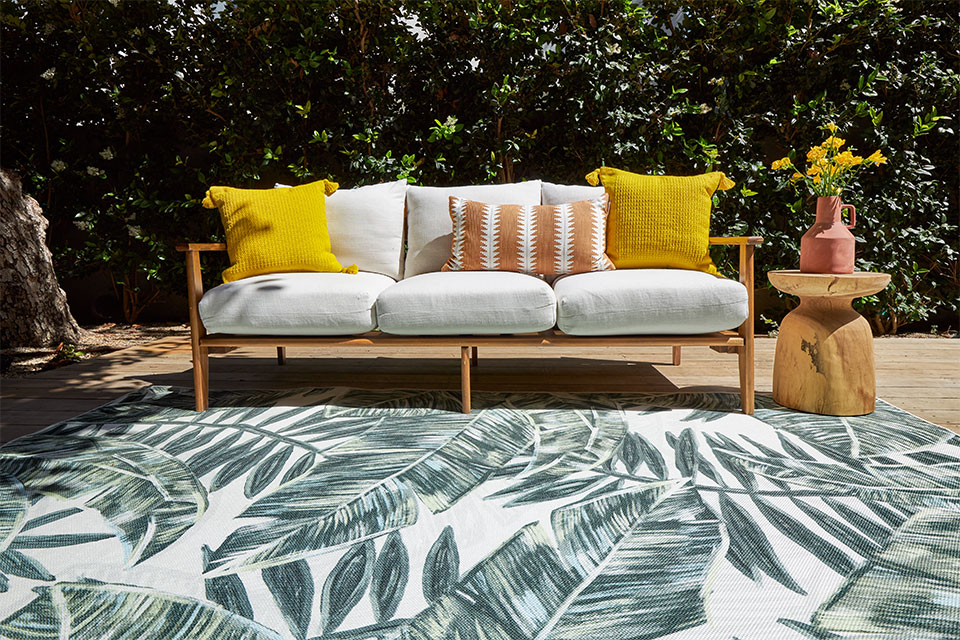 Green and white palm leaf rug with white couch and yellow pillows in patio