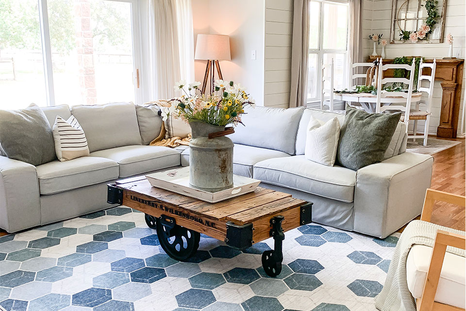 Blue and green hexagon patterned rug with light grey couch with wooden coffee table and flowers in living room