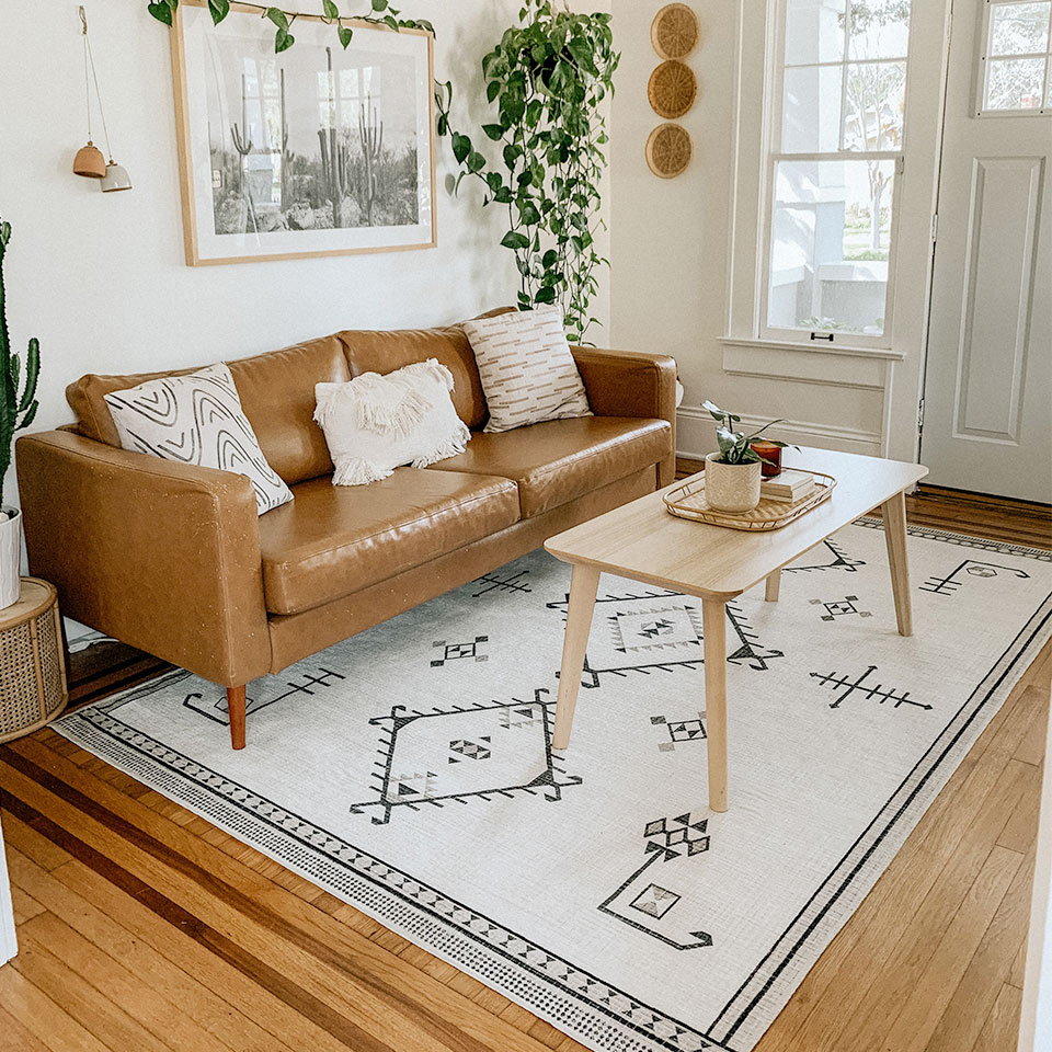 Black and white geometric rug under brown leather couch in small living room