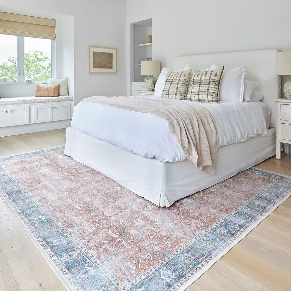 Coral farmhouse rug with blue border under a queen size white bed