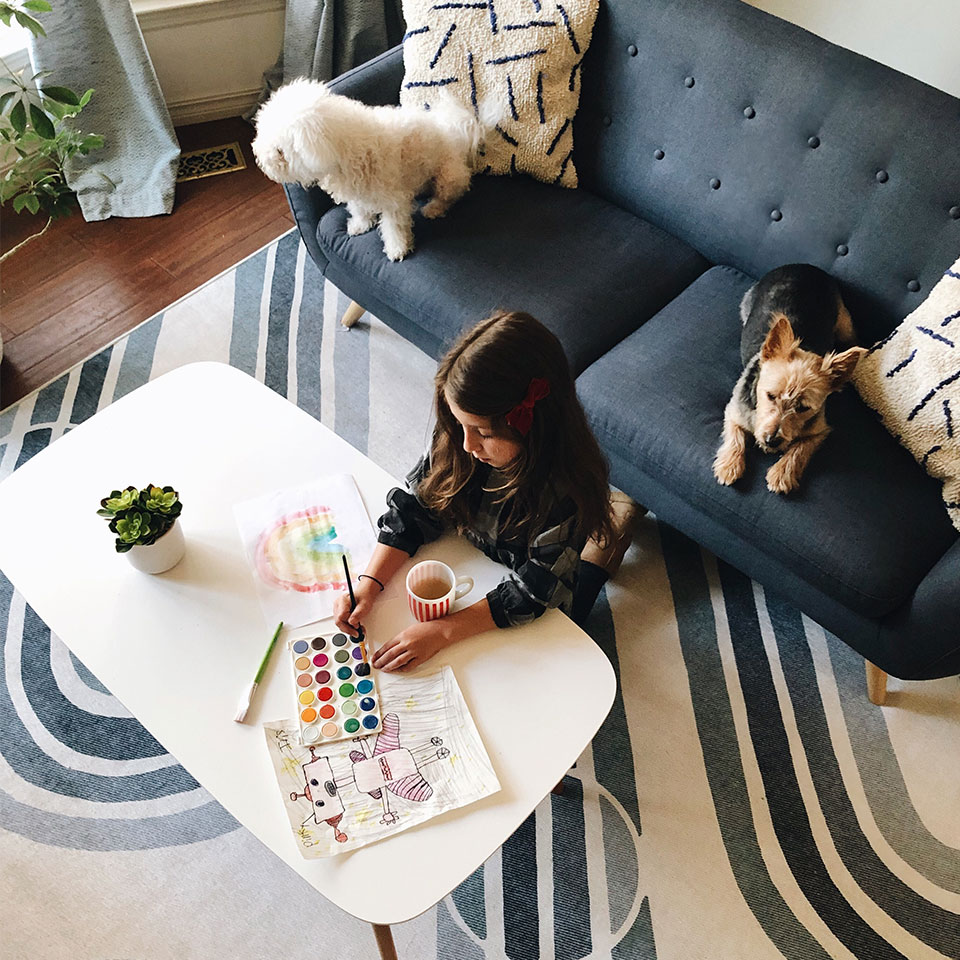 Girl painting in the living room on blue rug with two dogs