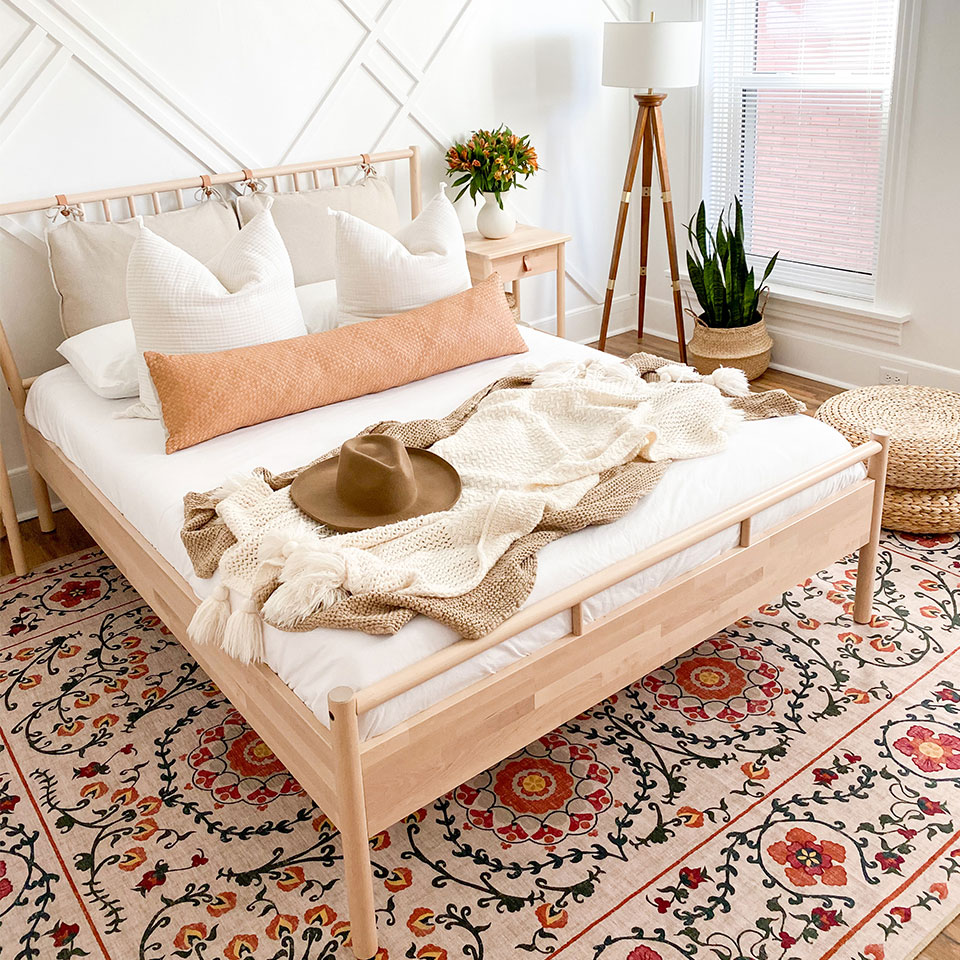 Orange floral rug in bedroom with wood bed with white sheets white pillows and white floor lamp