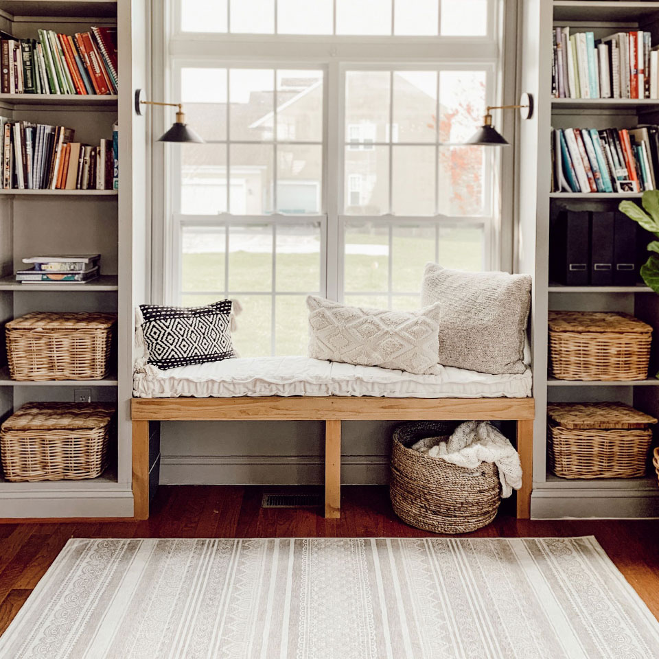 Reading nook by window with shelf and rattan baskets and grey striped rug