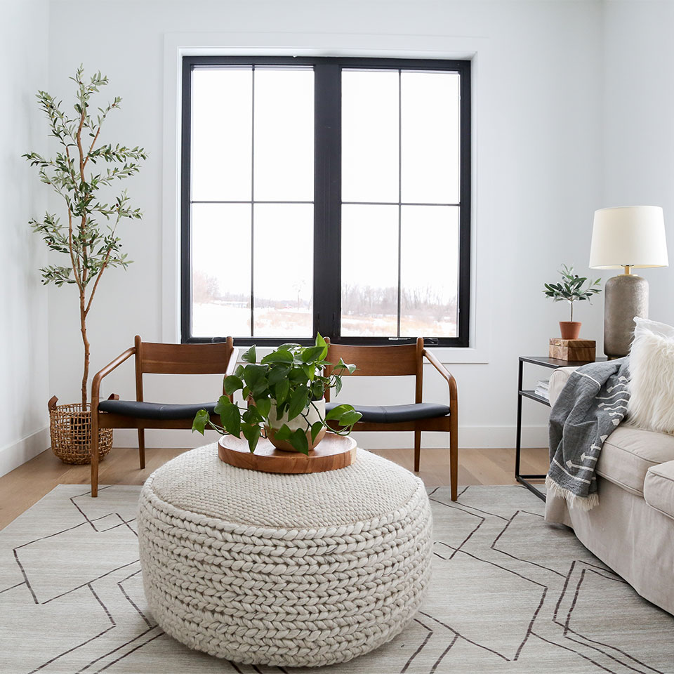 neutral living room design wooden armchairs houseplants woven ottoman