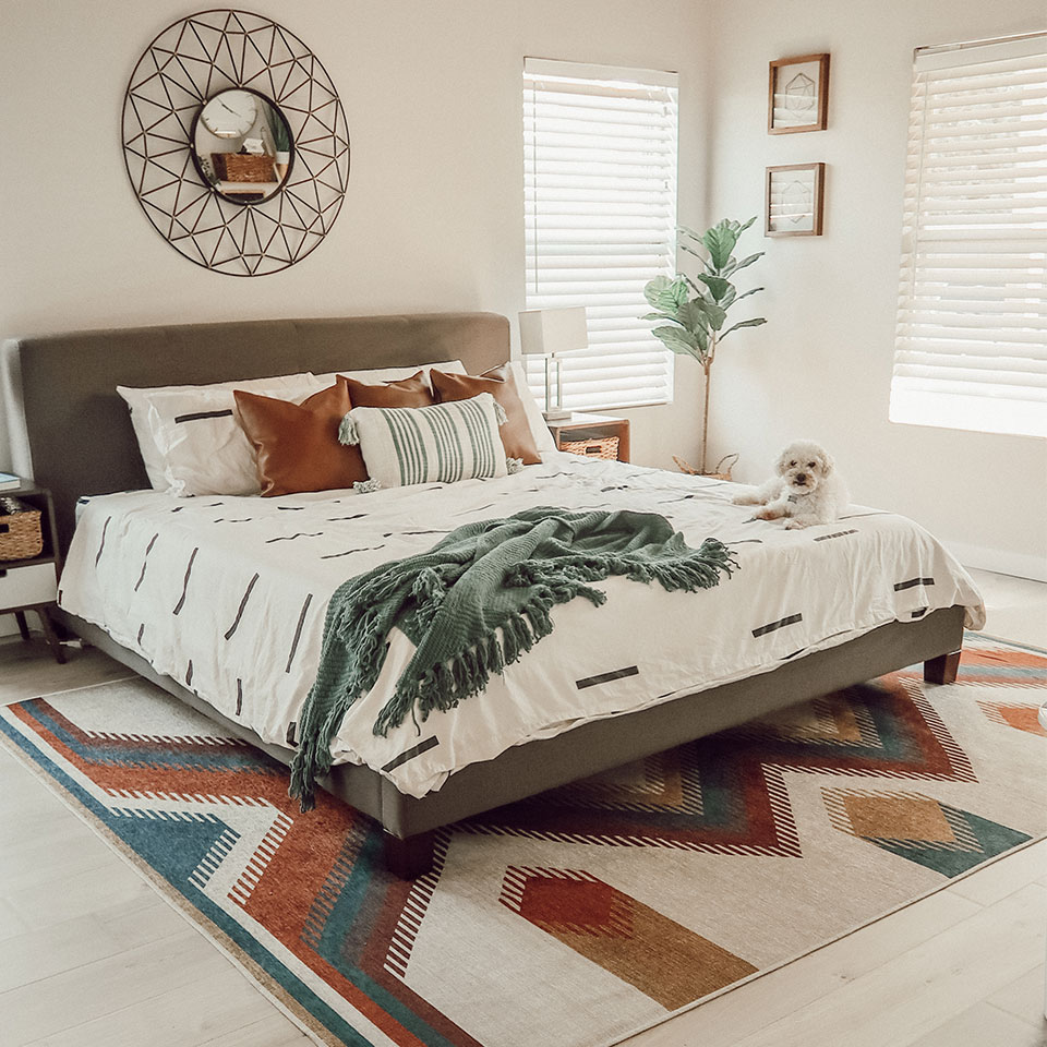 Colorful rug with brown and teal under queen bed in bedroom