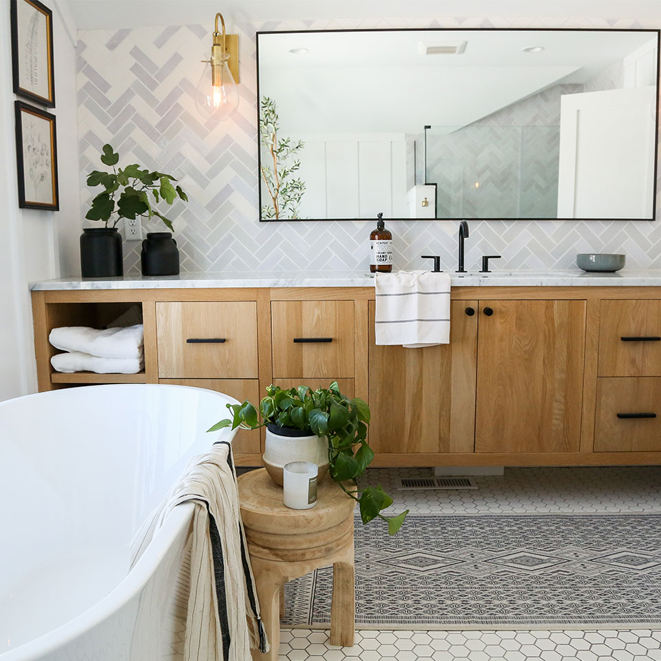 Wooden vanity with marble countertop by bathtub on black and white rug in bathroom