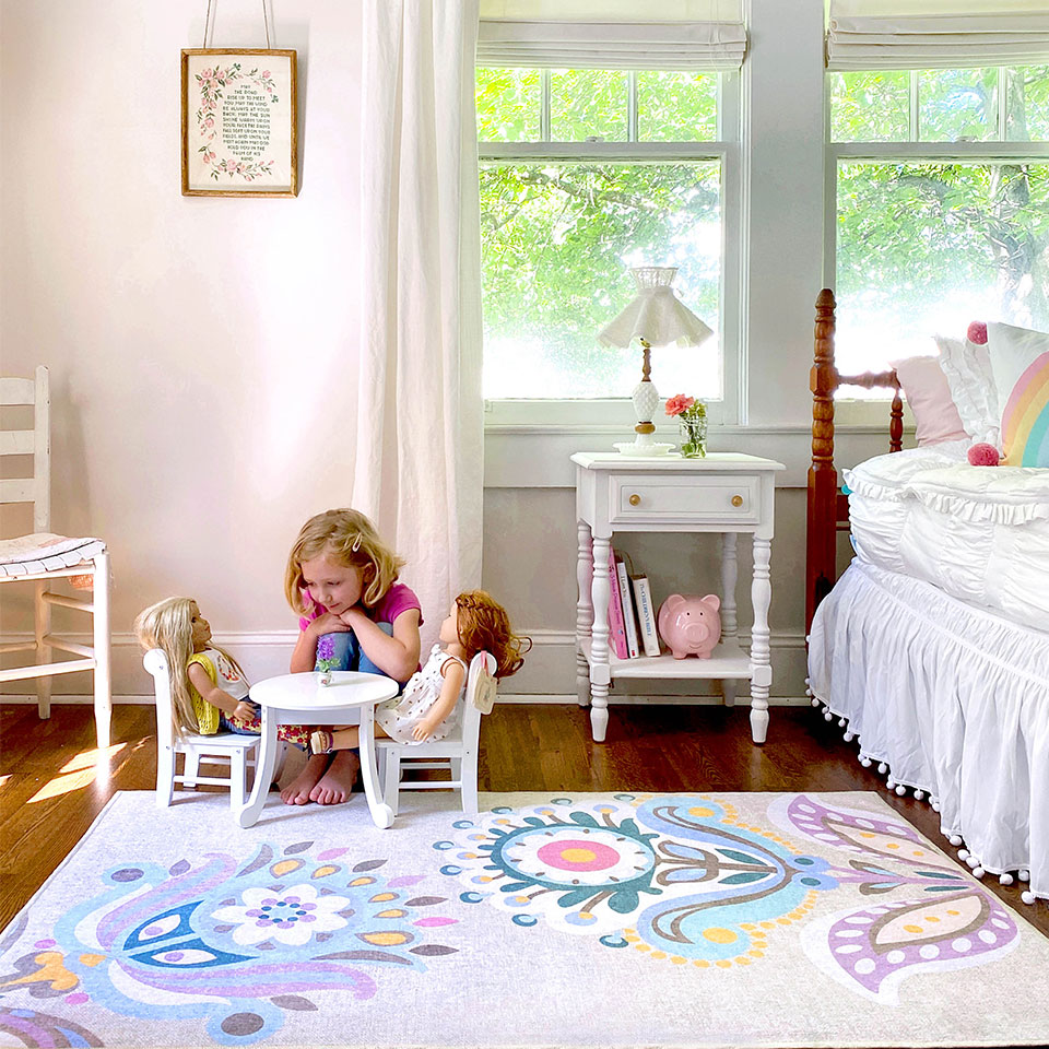 girl playing with dolls on colorful floral pastel rug