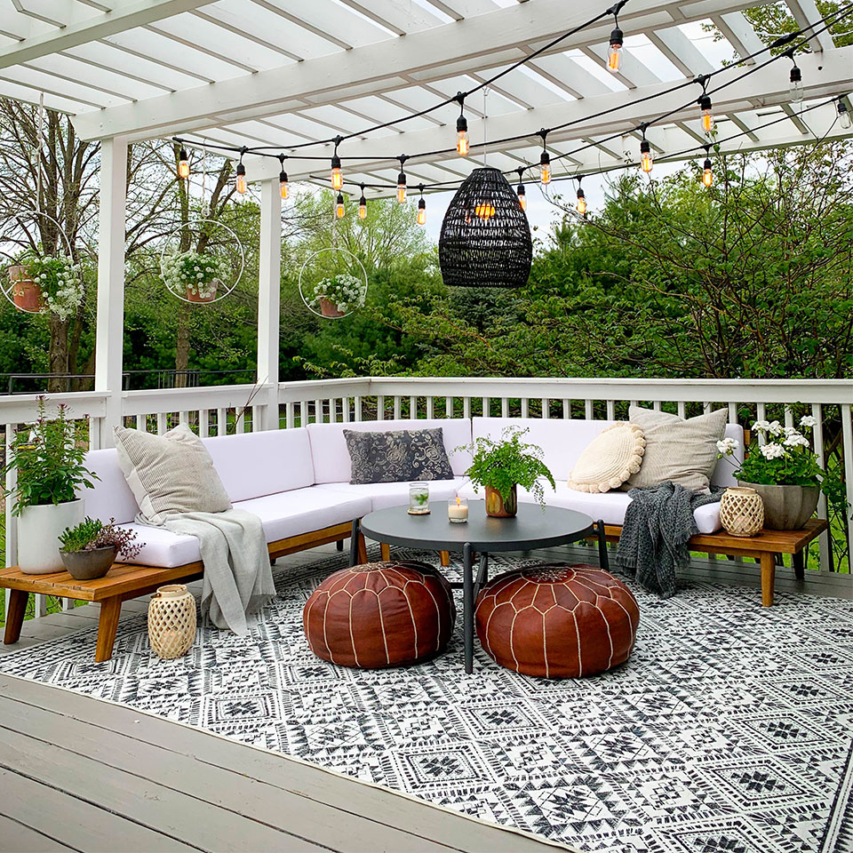 Black and white diamond outdoor rug in deck with white couch and brown leather ottoman with lights