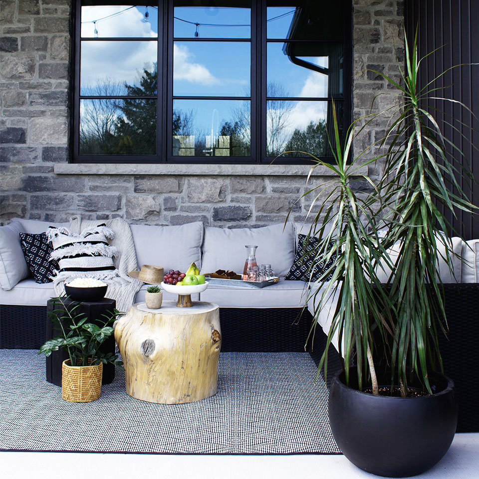 Black and white diamond outdoor rug with grey couch and black pillows and plants