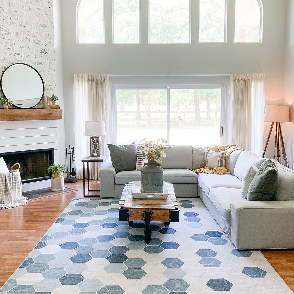 Blue and green hexagon patterned rug in living room with high ceiling and big windows and light grey couch
