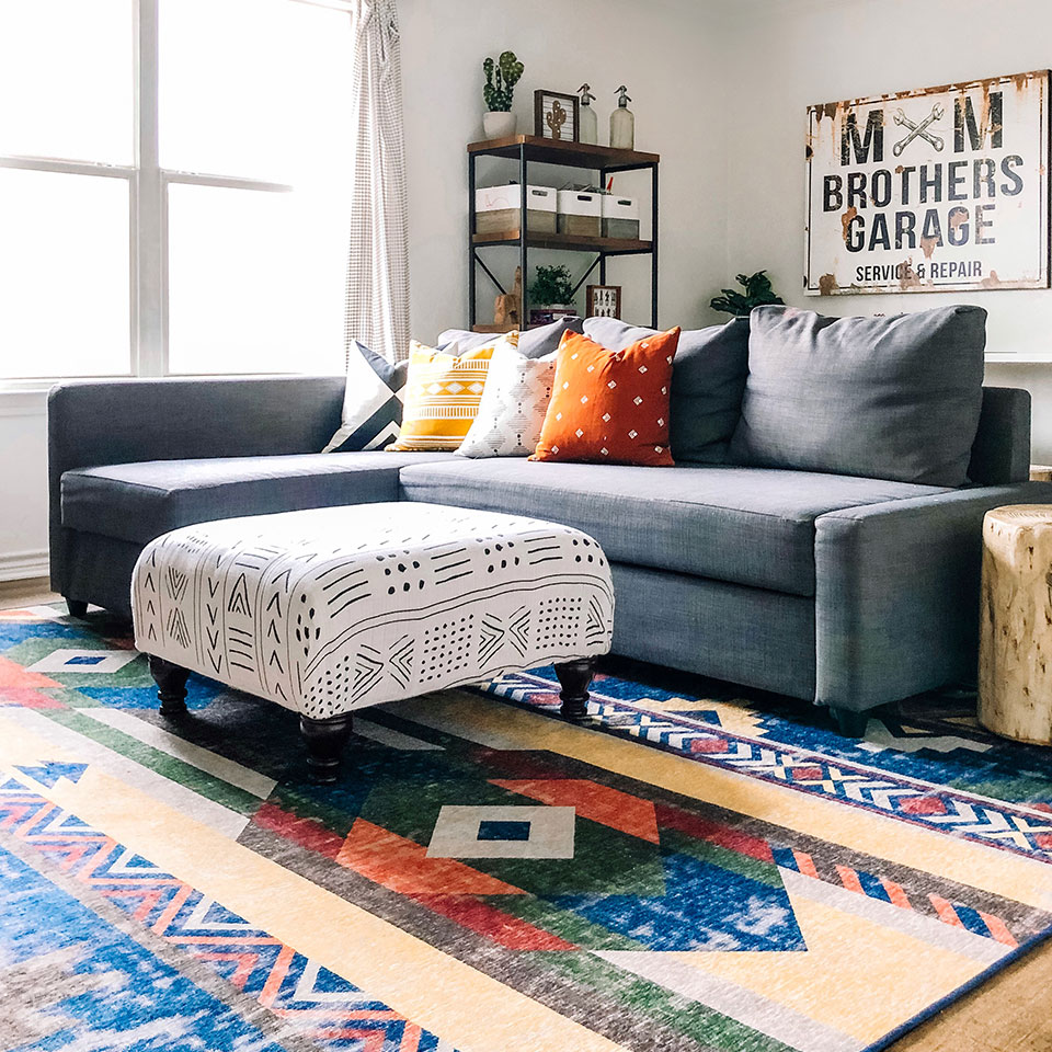 Colorful blue and yellow rug with grey couch black white ottoman and rust orange pillows