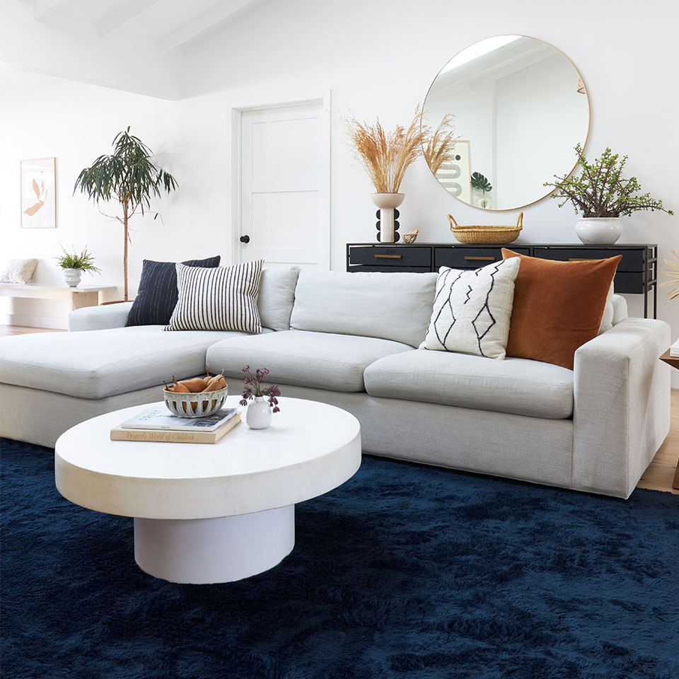 Blue fluffy plush rug in living room with grey couch white round table and round mirror