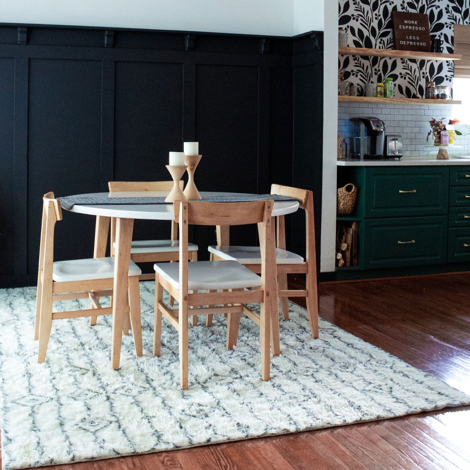 Geometric white plush rug with wooden dining table and chairs by kitchen with green cabinets