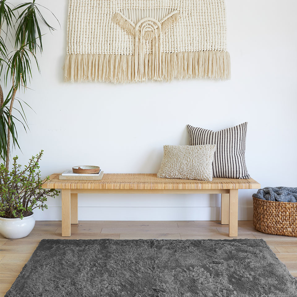 Grey plush rug with wooden bench and pillows and plants