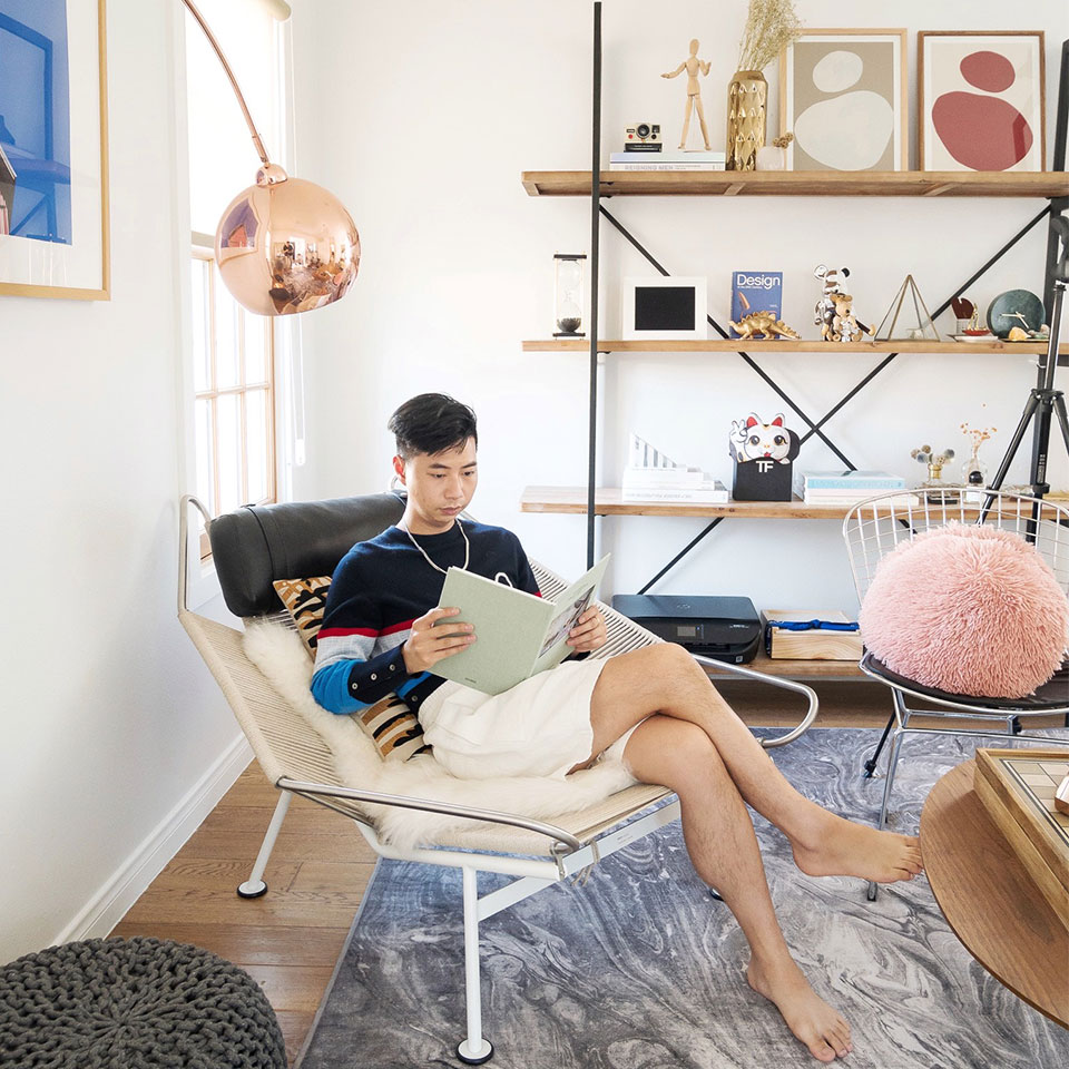 Tommy Lei reading in office with shelves, marble grey rug, pink pillow and grey ottoman.
