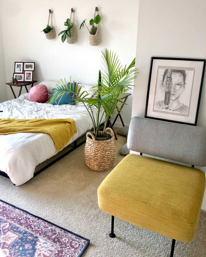 White queen bed with red persian rug and yellow and grey chair with hanging plants