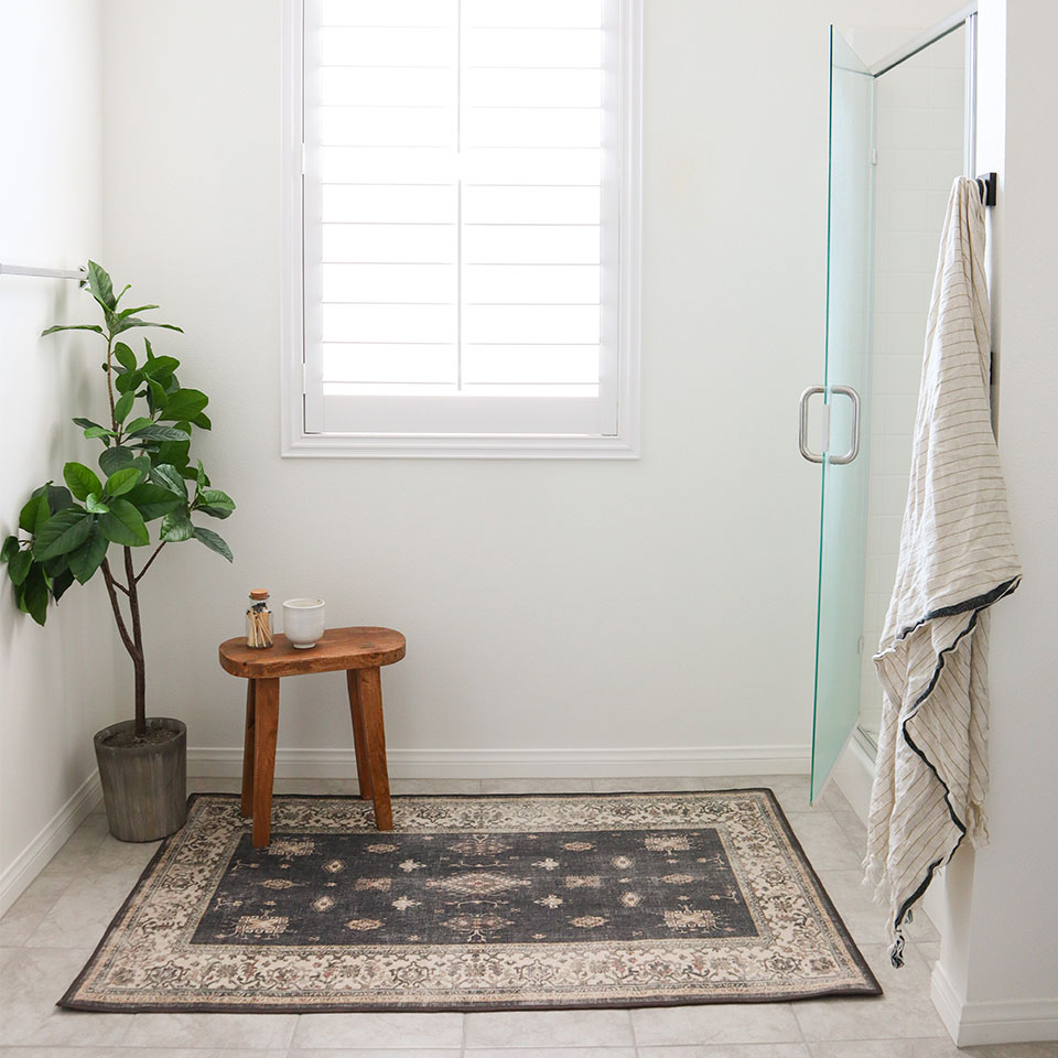 Bordered black farmhouse rug. with plant and stool in bathroom