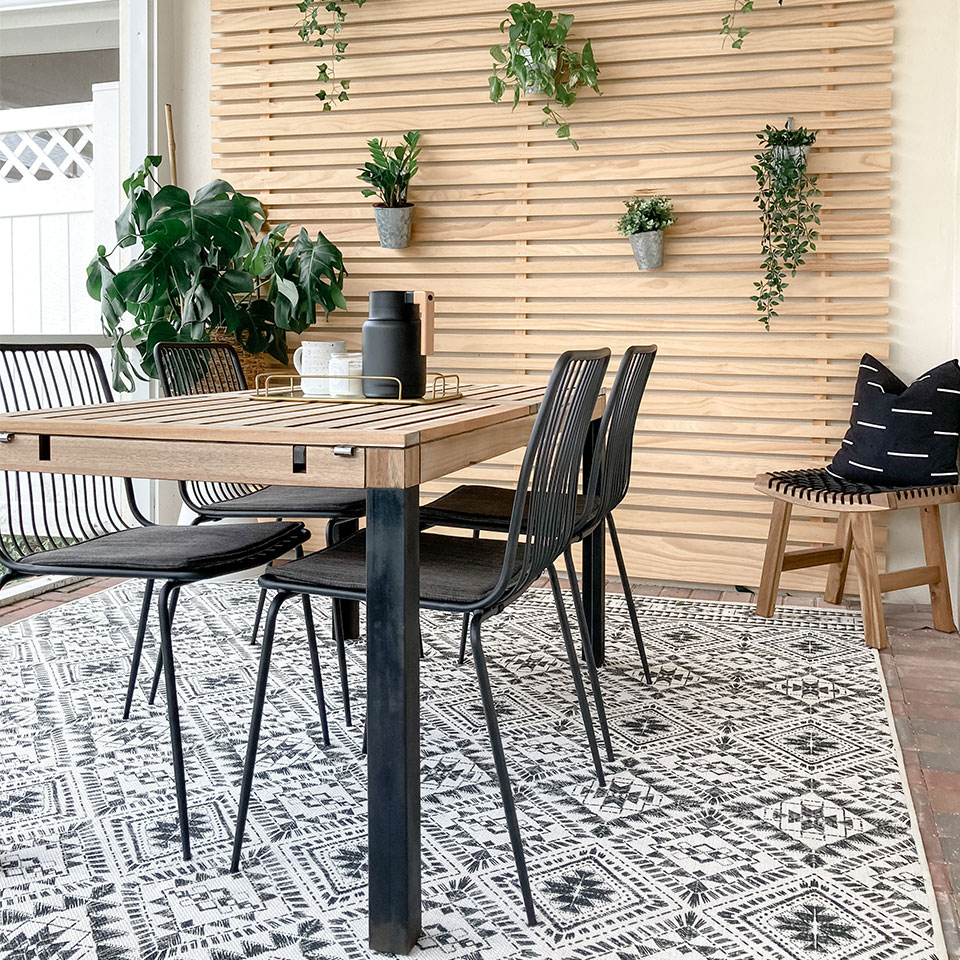 Black and white geometric bordered outdoor rug on a porch with dining table and chairs and hanging plants.