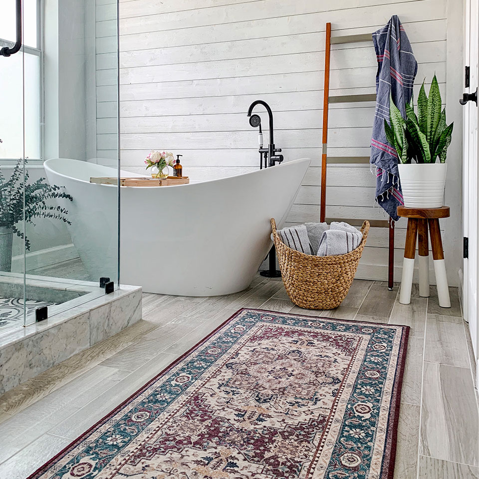 Red and blue Persian-style rug in a master bathroom with white and marble accents and a bathtub. 