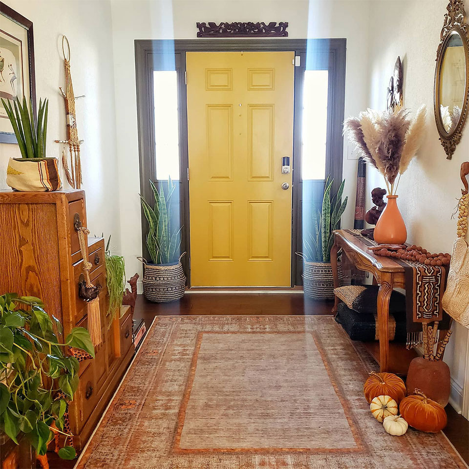Orange vintage rug with yellow door plants and pumpkin in entryway