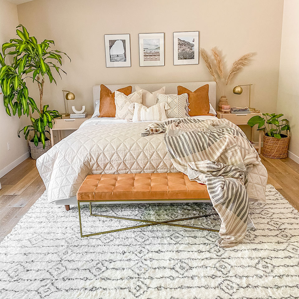 White geometric plush rug with brown leather bench under queen bed in bedroom with plants