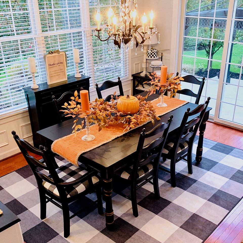 Black and white plaid dining room rug with orange runner pumpkin centerpiece and orange candles