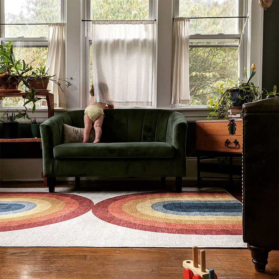 Rainblow rug in the living room with green couch plants and baby