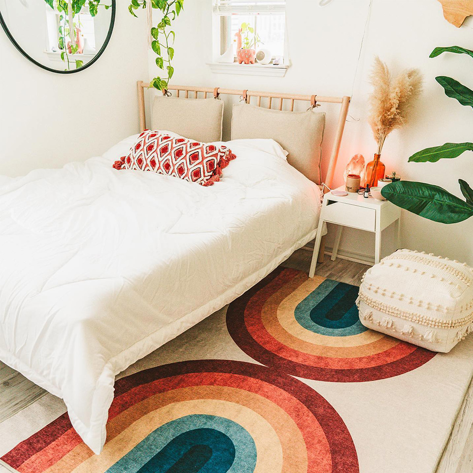 Rainbow rug in bedroom with hanging plant white bed and white pouf
