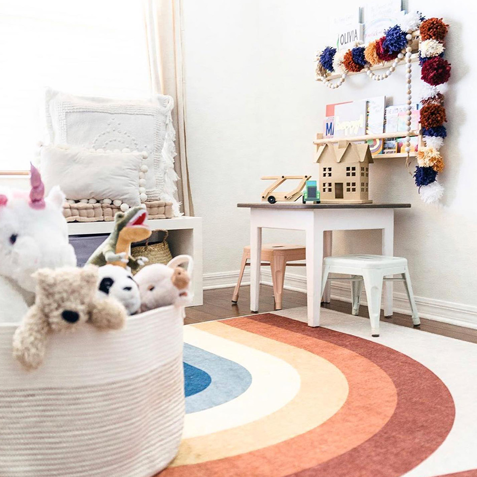 Rainbow rug in child's playroom with stuffed toy bin and toy house