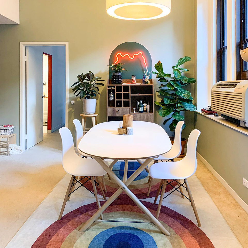 Rainbow rug in dining room with white midcentury modern dining table wood bar shelf and plants.