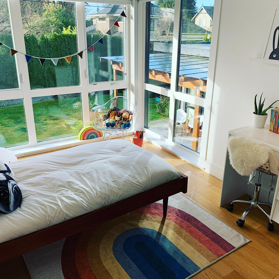 Rainbow rug in girls bedroom with white bed by big window