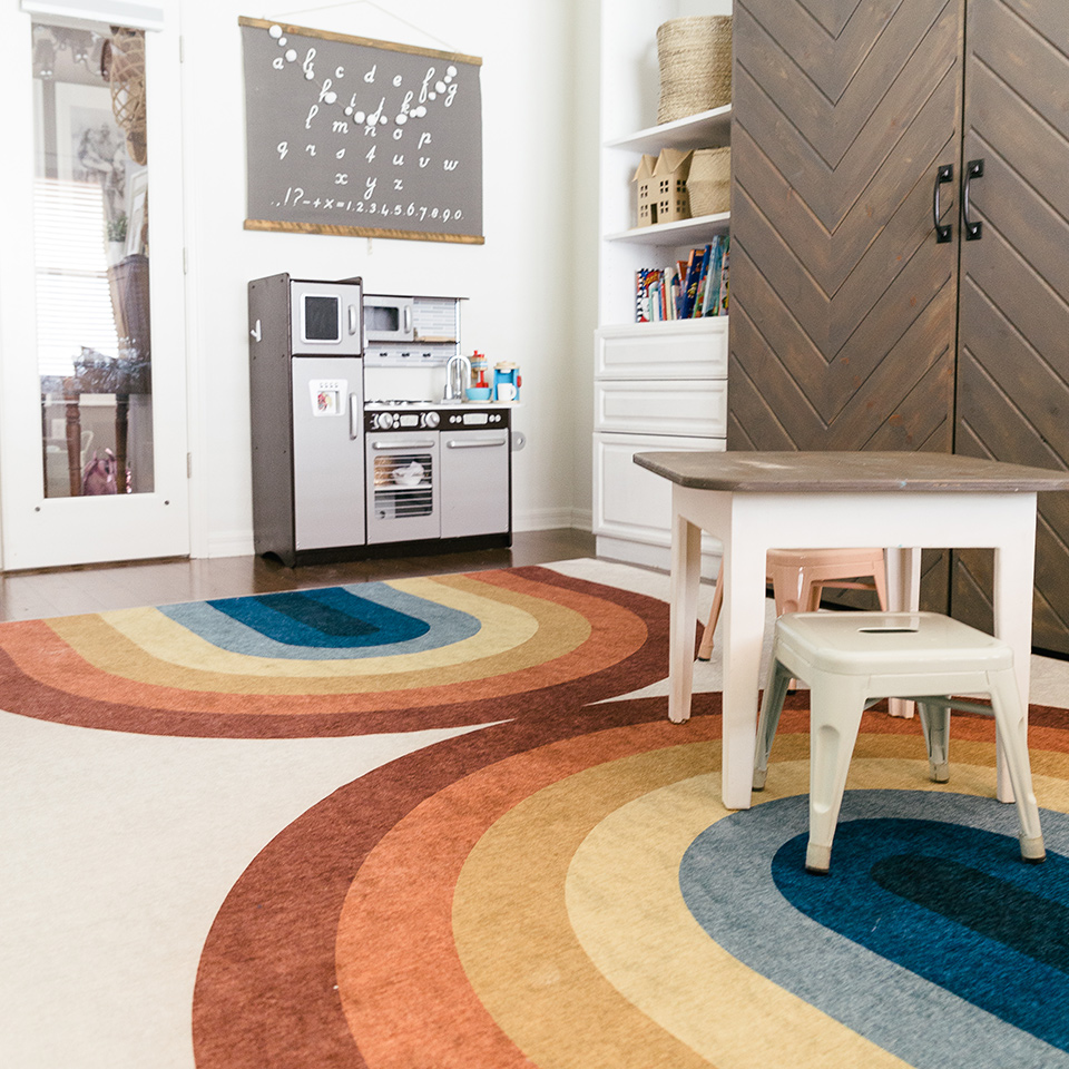 Rainbow rug in kids study and playroom with play kitchen and brown kids table