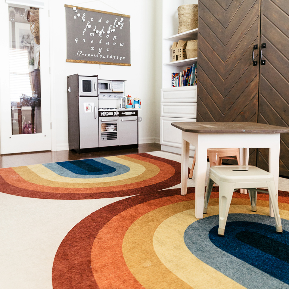 Rainbow rug in kids study and playroom with play kitchen and brown kids table