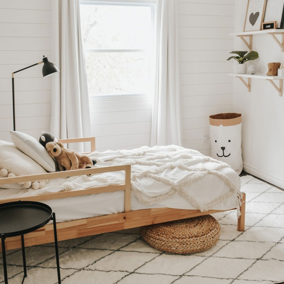 White kids room with white bed and brown and wood accents with white plush rug.