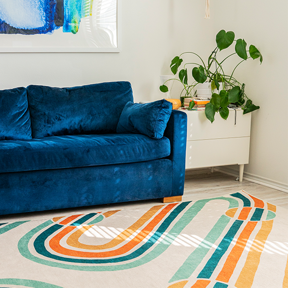 bright colored rug in living room with blue velvet sofa and plants