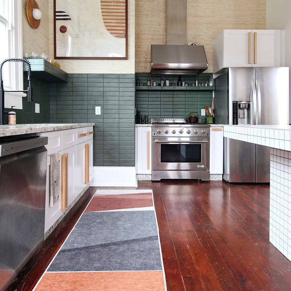 Red grey and orange rug on red wood floor with green walls in kitchen