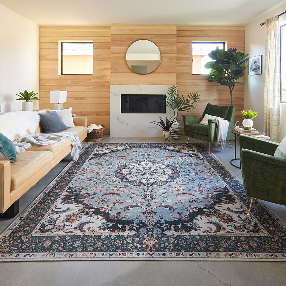 Sage green persian rug on concrete floor with brown leather couch green accent chair and wood wall in living room