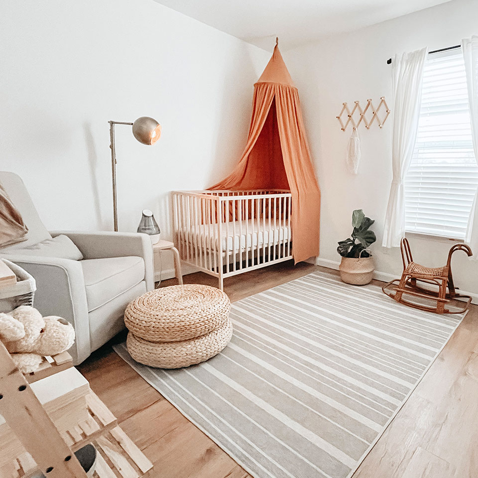 tan and white striped nursery rug with neutral decor and orange canopy