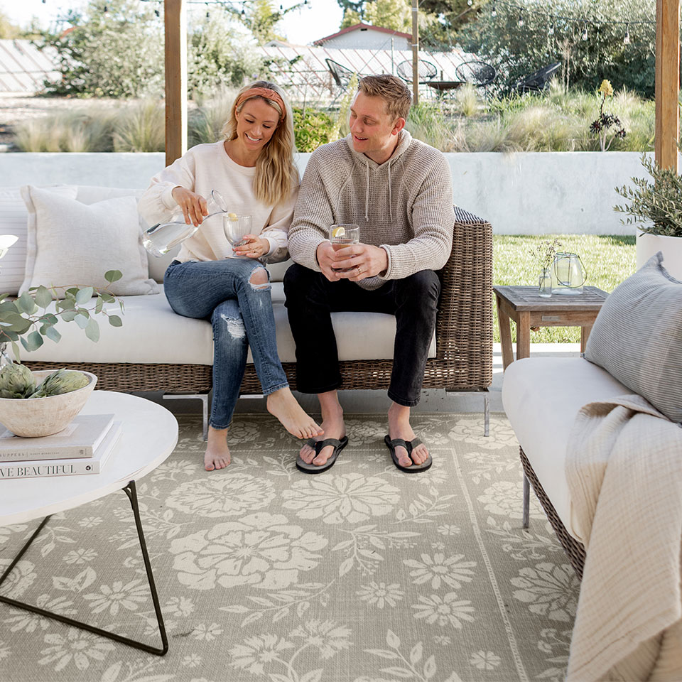 tan outdoor floral rug on patio with couple on sofa