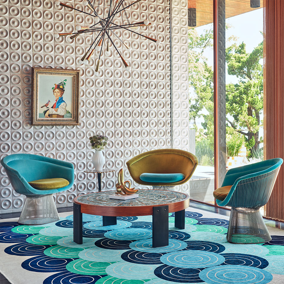 Blue and green jonathan adler rug with circle patterns in eclectic living room with round center table accent chairs and textured wall